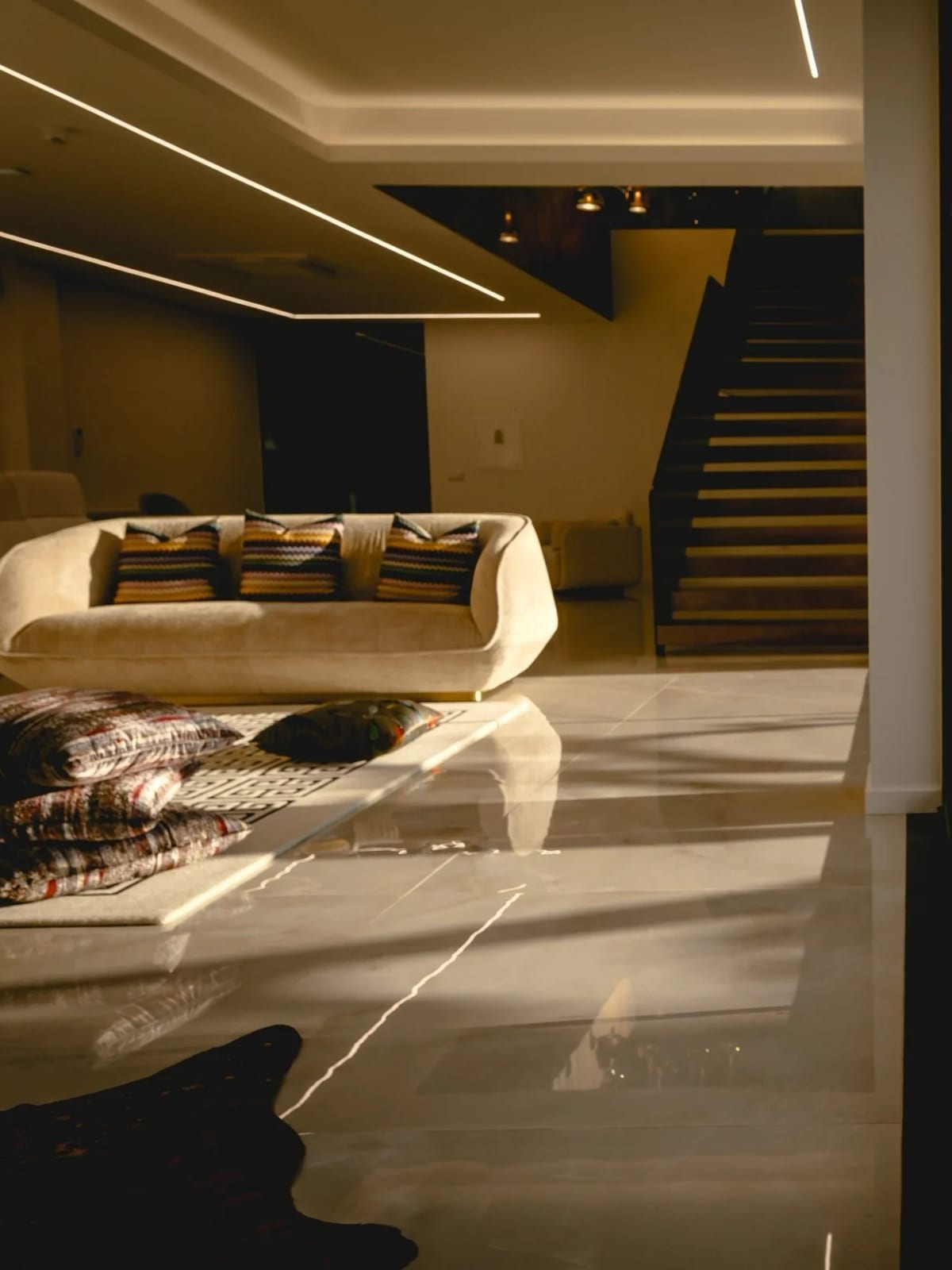A pale curved sofa with patterned cushions on polished marble, a lit staircase behind at night