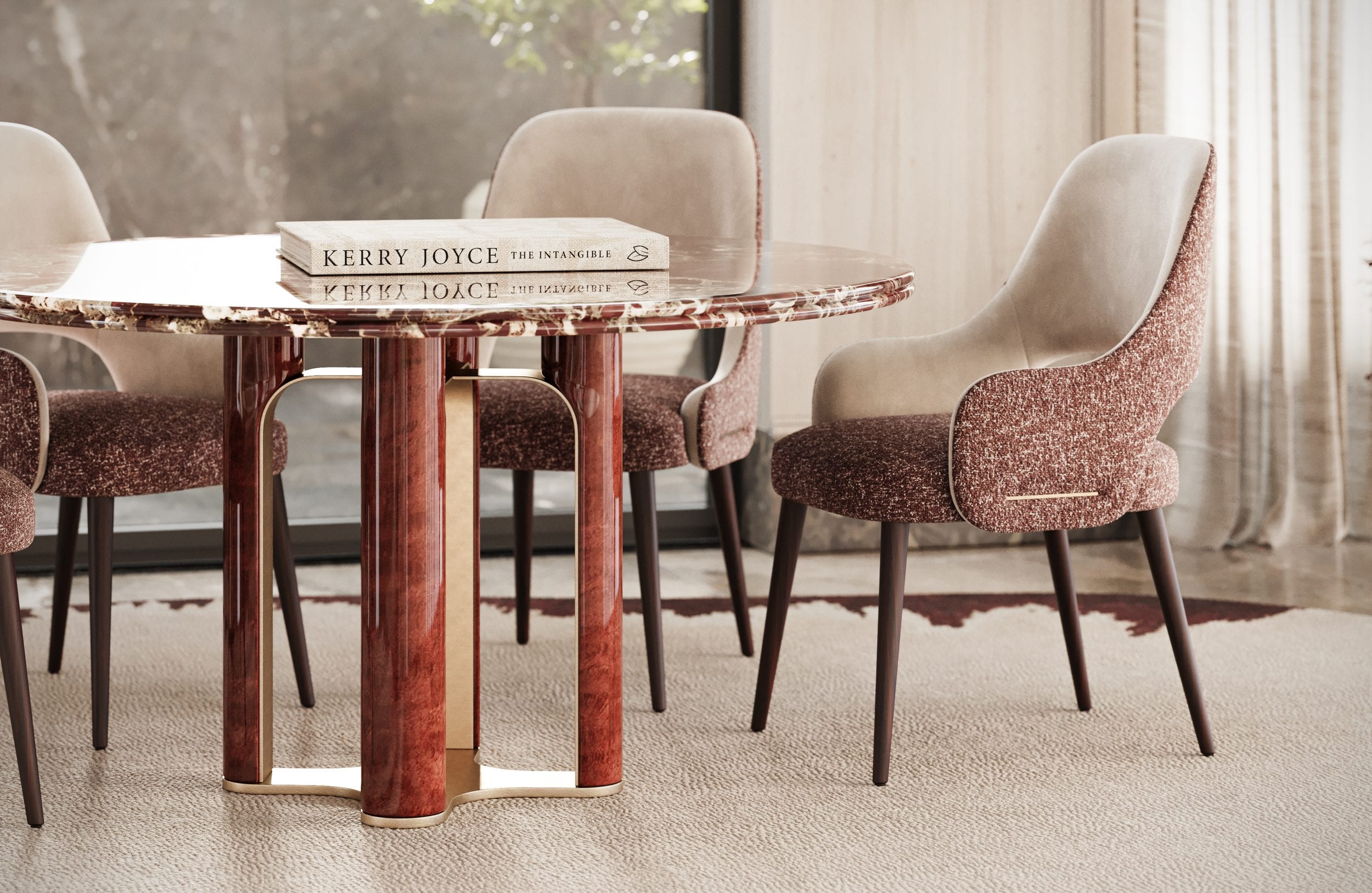 The round marble table with books laid on it, ringed by upholstered chairs before a window